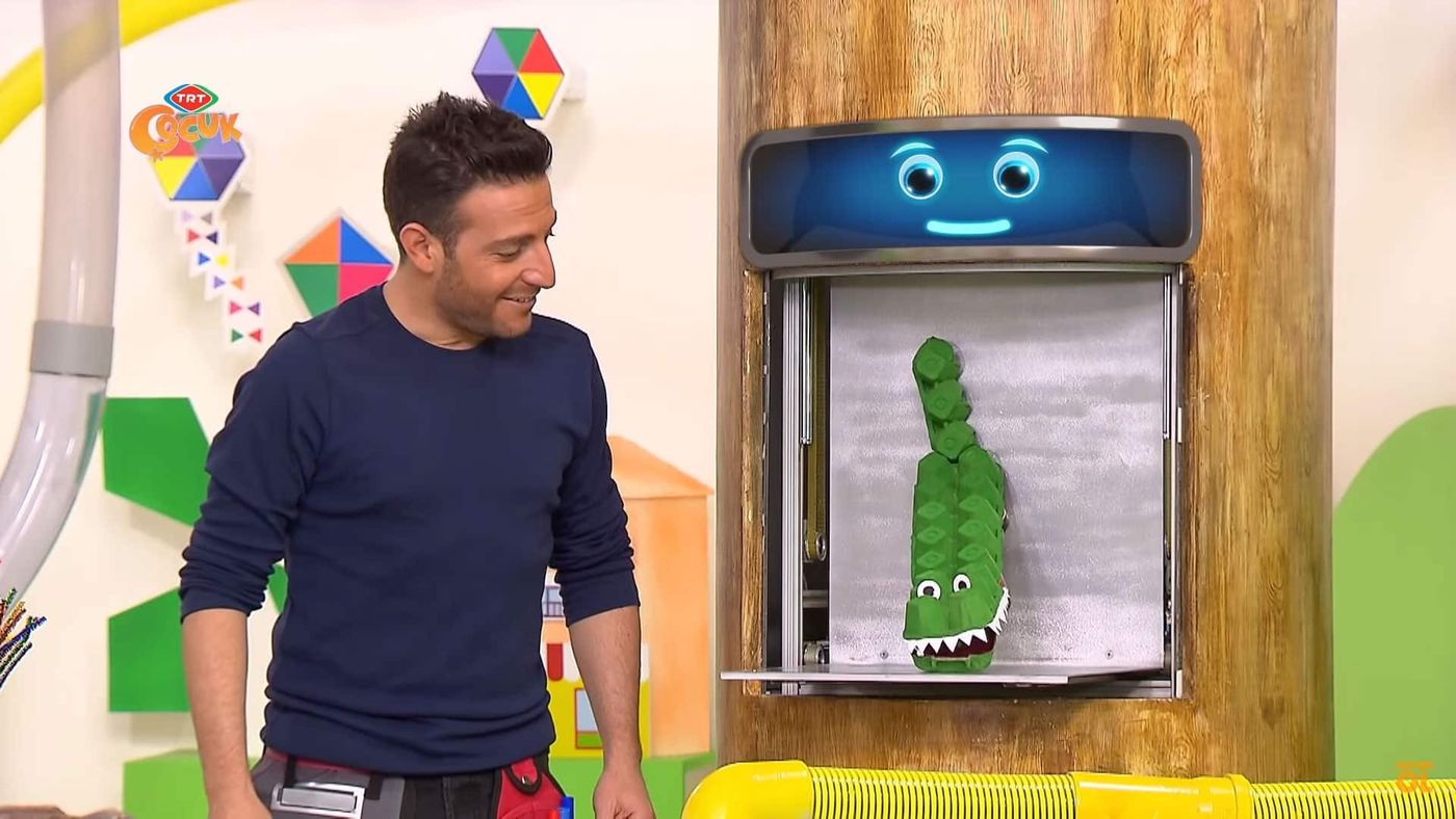 Programdan kare: sunucu, ekranlı dolapta duran yeşile boyanmış yumurta kolisinden timsaha bakıyor