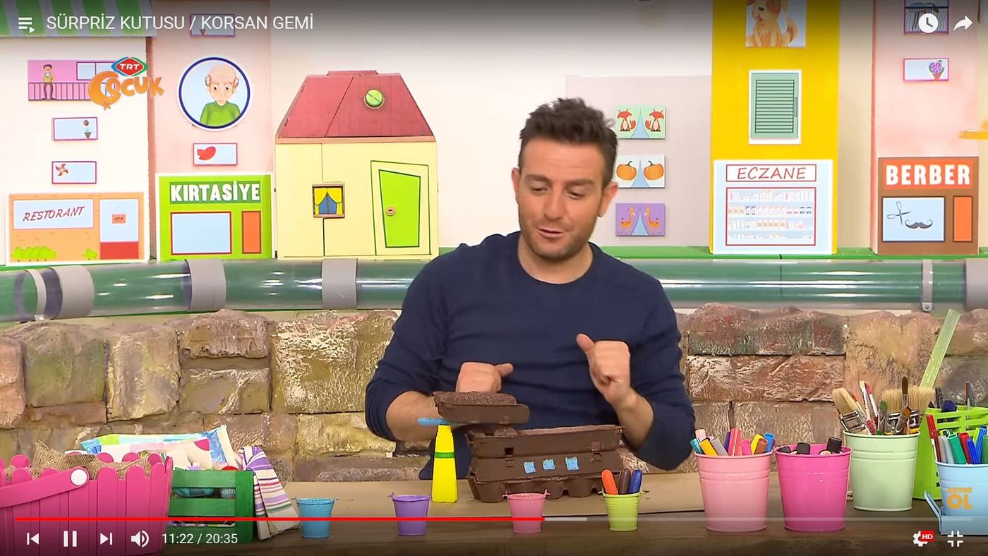 Program kaydından kare: sunucu masada yumurta kolisinden gemi gövdesi üzerinde çalışıyor