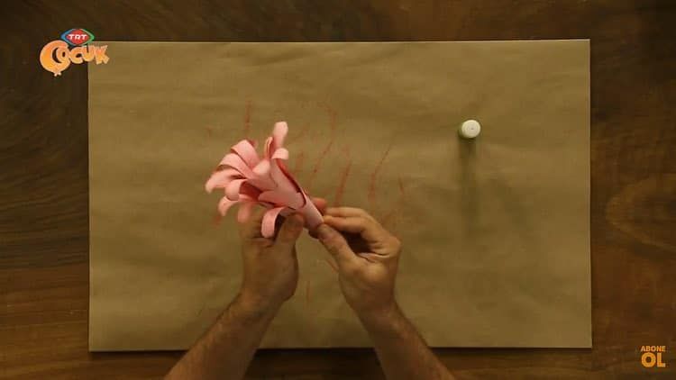 El biçiminde kesilmiş pembe kağıt rulo yapılarak çiçeğe dönüştürülüyor