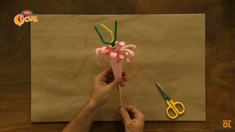 Pembe kağıt çiçek yeşil tüylü telden sapa takılıyor, yanında makas