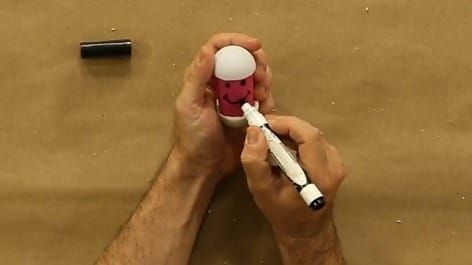 Pembe kağıtla sarılmış yumurta biçimli hacıyatmaza keçeli kalemle yüz çiziliyor