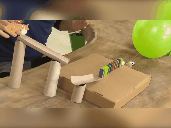 Balon Patlatma düzeneği: tuvalet kağıdı rulosu kuleler, karton rampa, renkli domino taşları ve yeşil balon