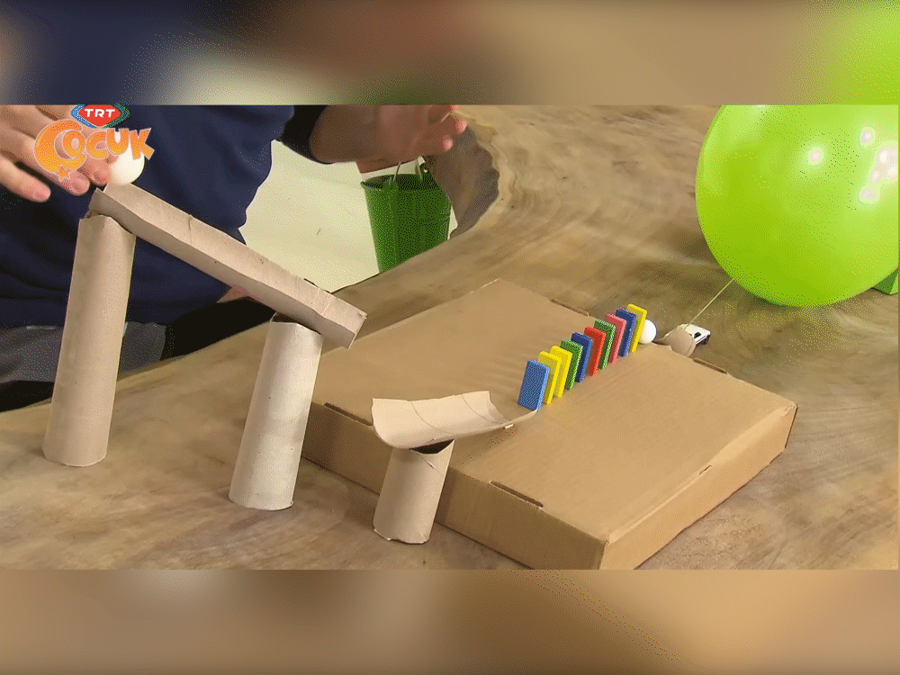 Balon Patlatma düzeneği: tuvalet kağıdı rulosu kuleler, karton rampa, renkli domino taşları ve yeşil balon