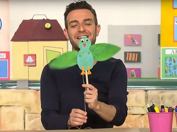 Kuş kukla: sunucu çubuğa takılı, yeşil kanatlı mavi kağıt kuşu kanatlarını oynatarak gösteriyor