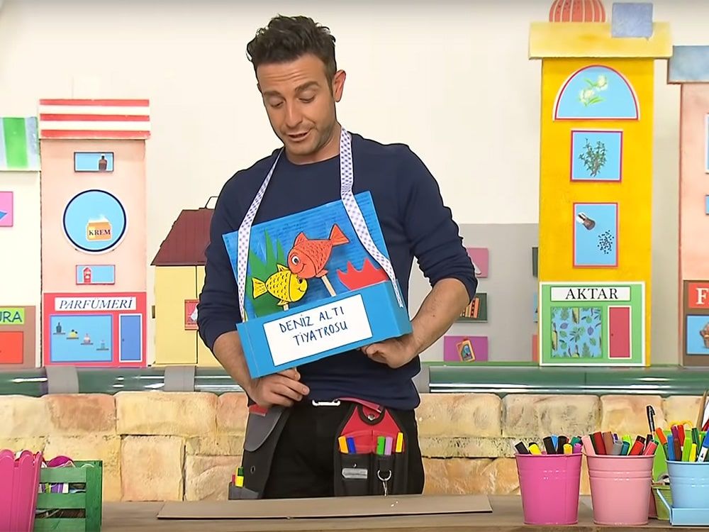 Televizyon programından kare: sunucu boynuna astığı deniz altı tiyatrosu kutusunu gösteriyor