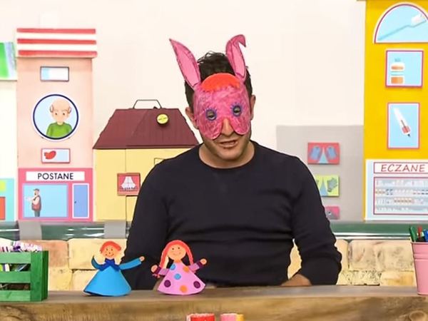 Karton Kardeşler televizyon programından kare: pembe tavşan maskesi takan sunucu, önünde iki koni bebek