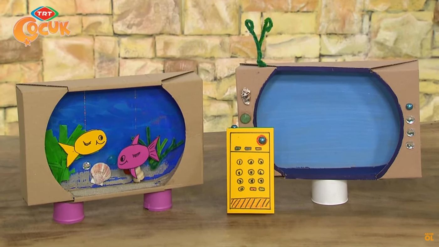 Bitmiş kutu akvaryum, yanında aynı yöntemle yapılmış karton televizyon ve sarı kumanda