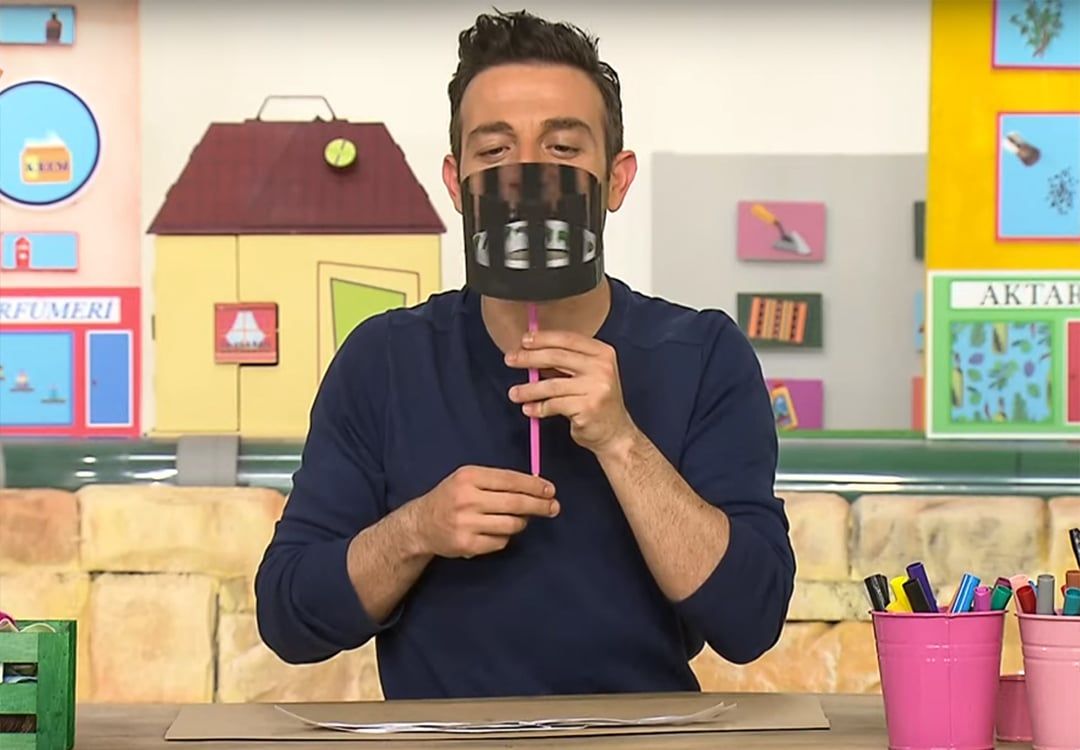 Zoetrope program karesi: sunucu çubuğa takılı yarıklı siyah silindiri yüzüne tutup içinden bakıyor
