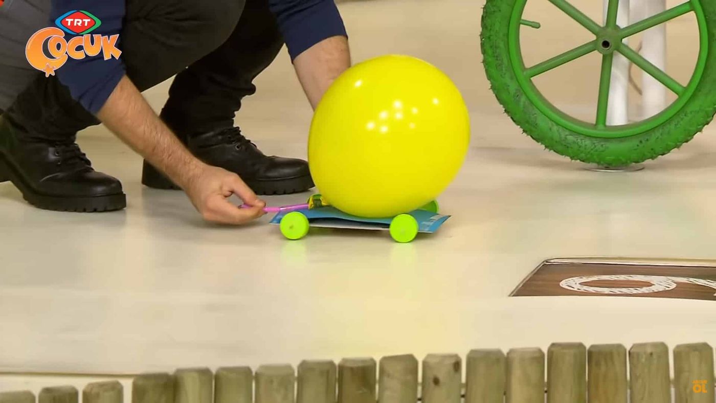 Şişirilmiş sarı balonlu araba stüdyo zemininde, bir el pipetin ucundan tutarak bırakmaya hazırlanıyor