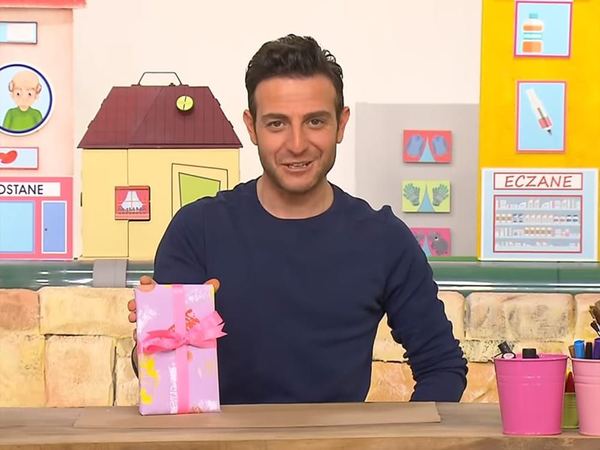 Baskı Çalışması: sunucu renkli baskı desenli leylak kağıtla sarılmış, pembe kurdeleli hediye paketini gösteriyor