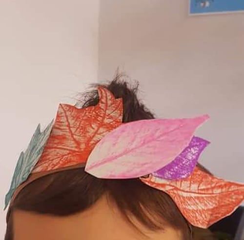 Başa takılı tacın üstünde pembe, turuncu ve mor kopyalanmış kağıt yapraklar yakından