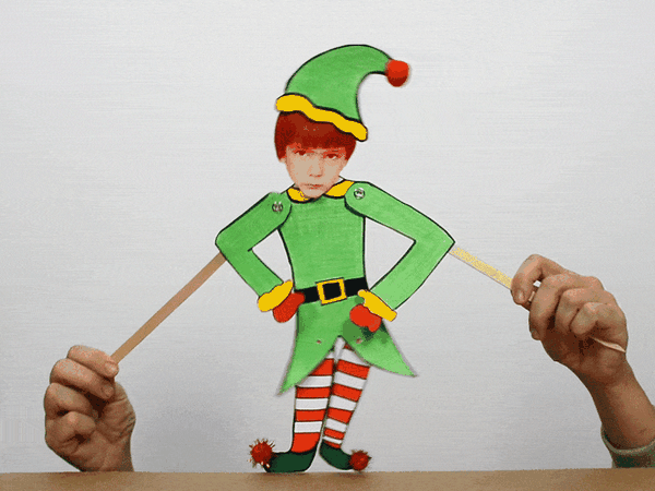 Elf kukla: yeşil şapkalı, çizgili çoraplı karton elf, iki elle kollarına bağlı çubuklarla oynatılıyor