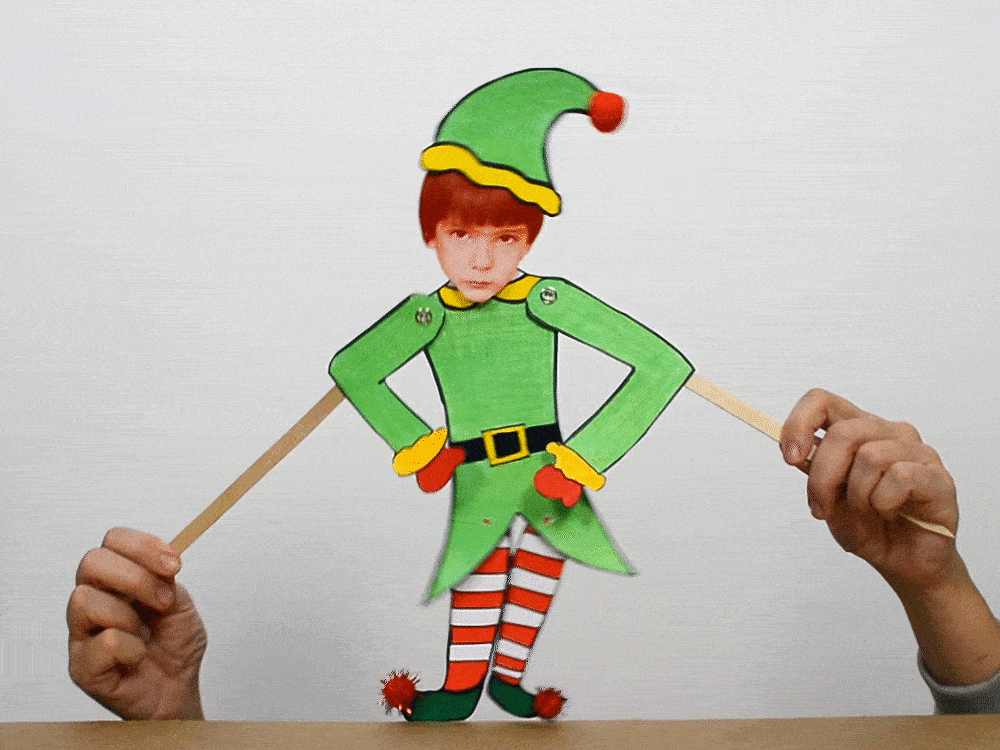 Elf kukla: yeşil şapkalı, çizgili çoraplı karton elf, iki elle kollarına bağlı çubuklarla oynatılıyor