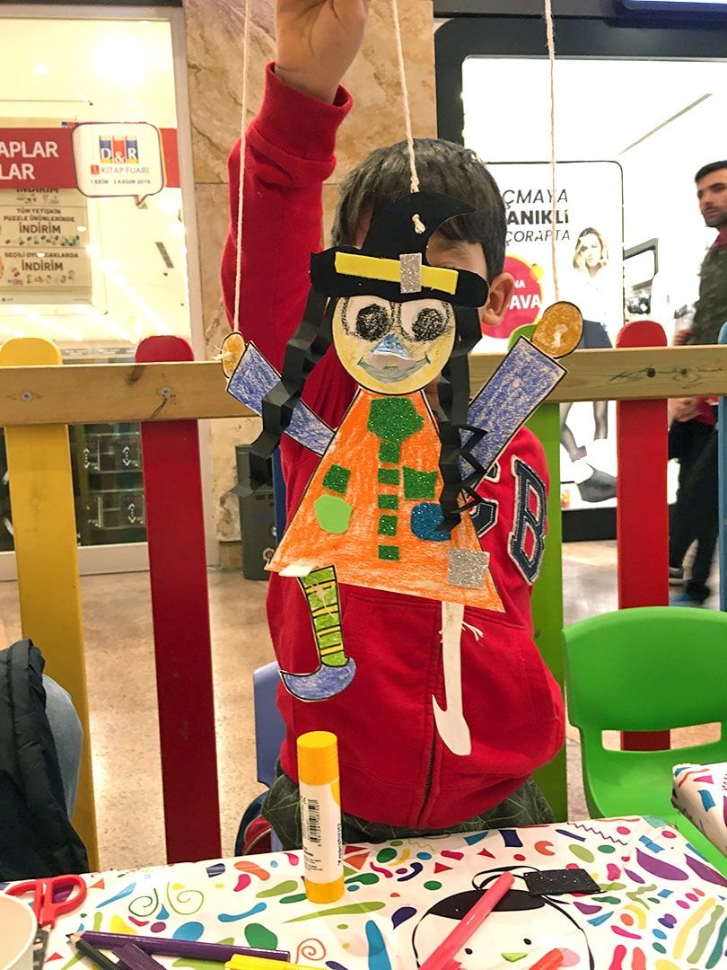 Atölye masasında turuncu elbiseli, gri yüzlü kağıt cadı kukla havaya kaldırılmış