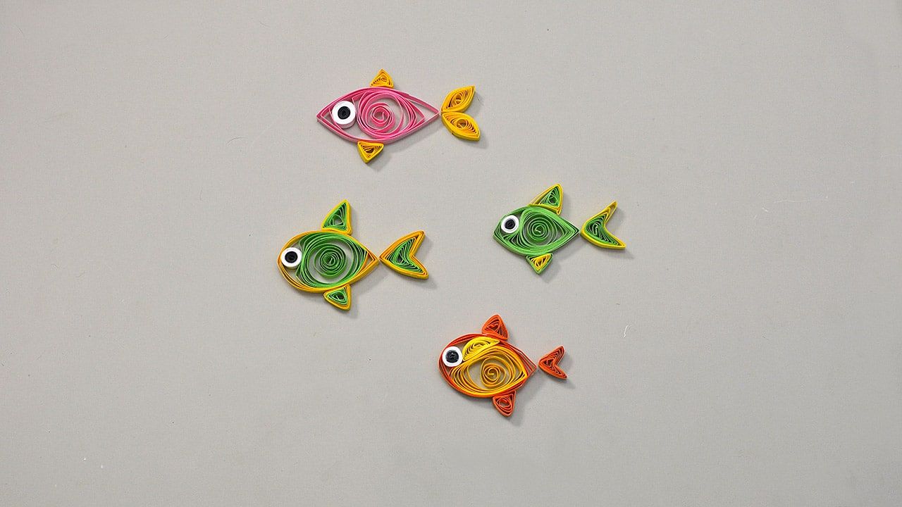 Kağıt dolama tekniğiyle yapılmış pembe, yeşil ve turuncu dört küçük quilling balık, oynar gözlü