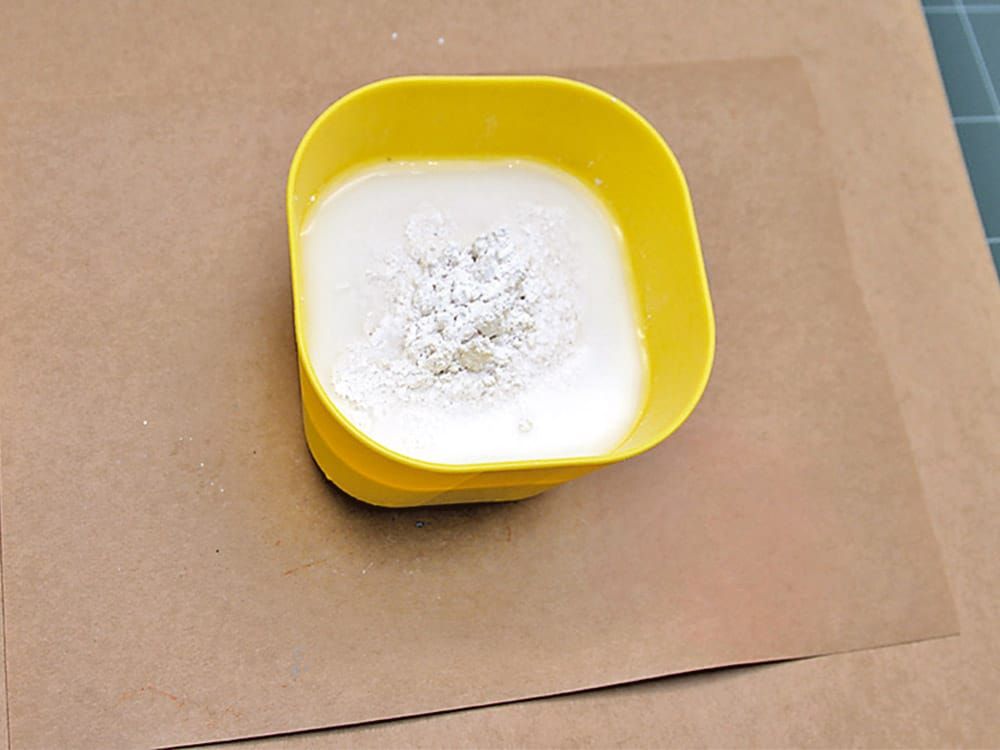 Sarı plastik kabın içinde suyla karıştırılmaya hazır beyaz toz alçı, kraft kağıt üzerinde