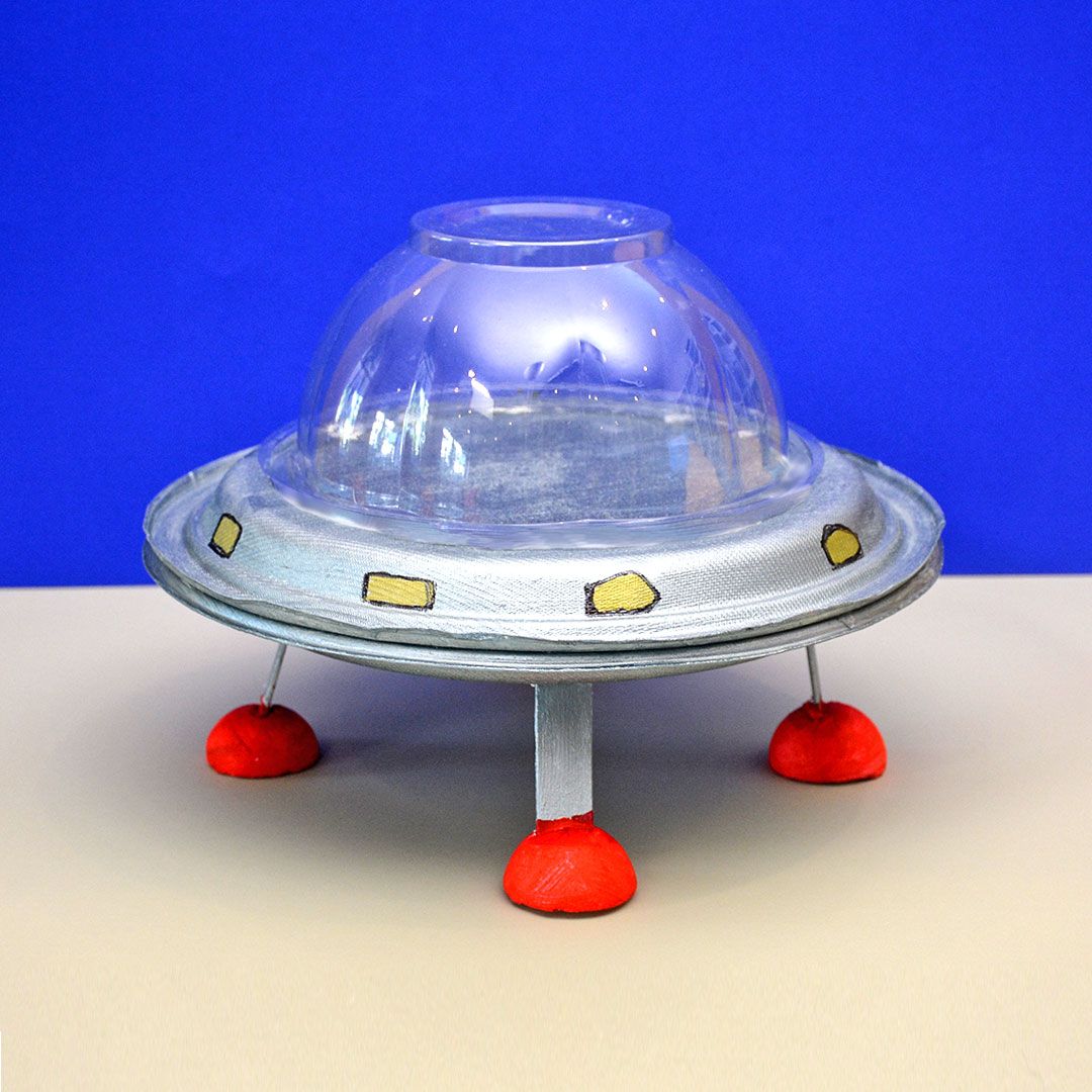 İki karton tabak ve şeffaf plastik kubbeden yapılmış gümüş UFO, sarı pencereli ve kırmızı ayaklı
