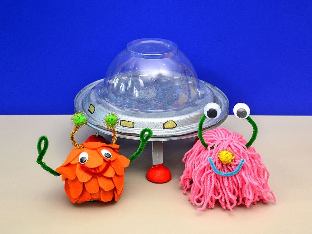 UFO ve sevimli uzaylılar: karton tabak ve şeffaf kubbeli gümüş UFO önünde turuncu ve pembe uzaylılar