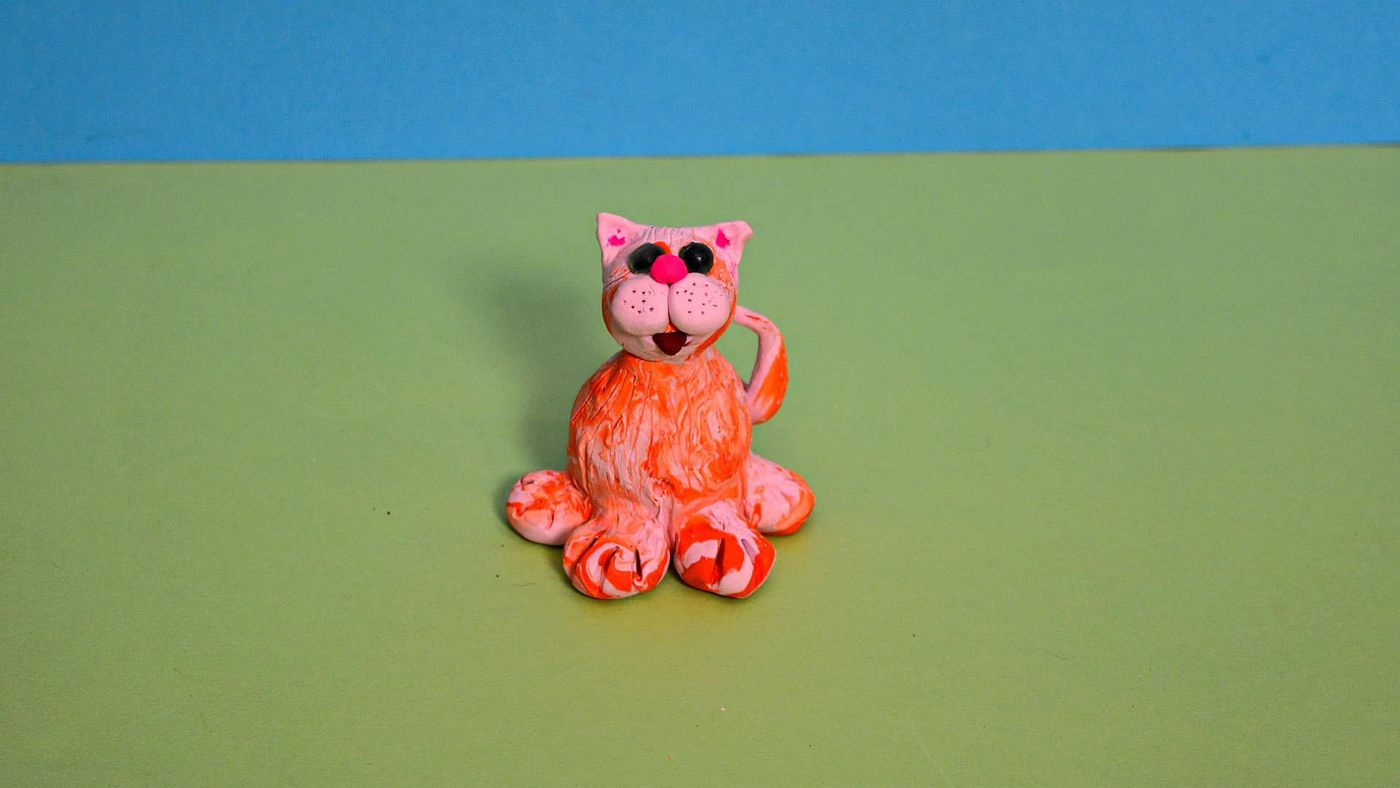 Turuncu-beyaz mermer desenli polimer kil kedi, pembe yüzü ve kıvrık patileriyle oturuyor