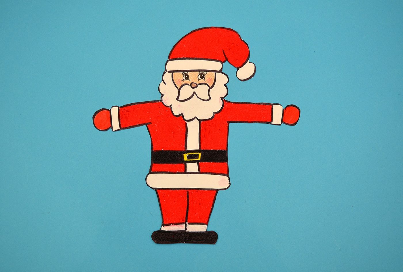 Kırmızı giysili, beyaz sakallı, kolları açık Noel Baba çizimi boyanıp kesilmiş, mavi zemin üstünde
