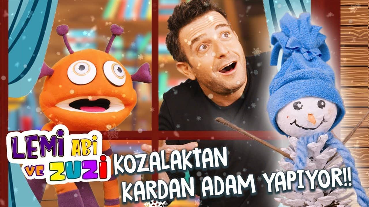 Kozalak kardan adam videosunun kapağı: sunucu, turuncu uzaylı kukla ve mavi bereli kozalak kardan adam