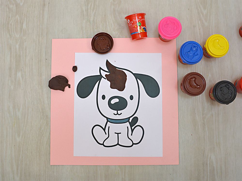 Köpek çiziminin kafasına kahverengi oyun hamuru parçaları bastırılmaya başlanmış